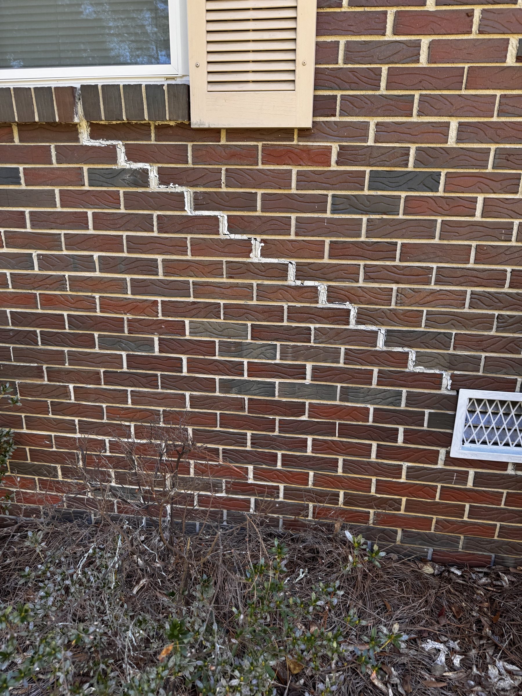 Stair-step crack running diagonally through a brick veneer wall, joints filled with sealant