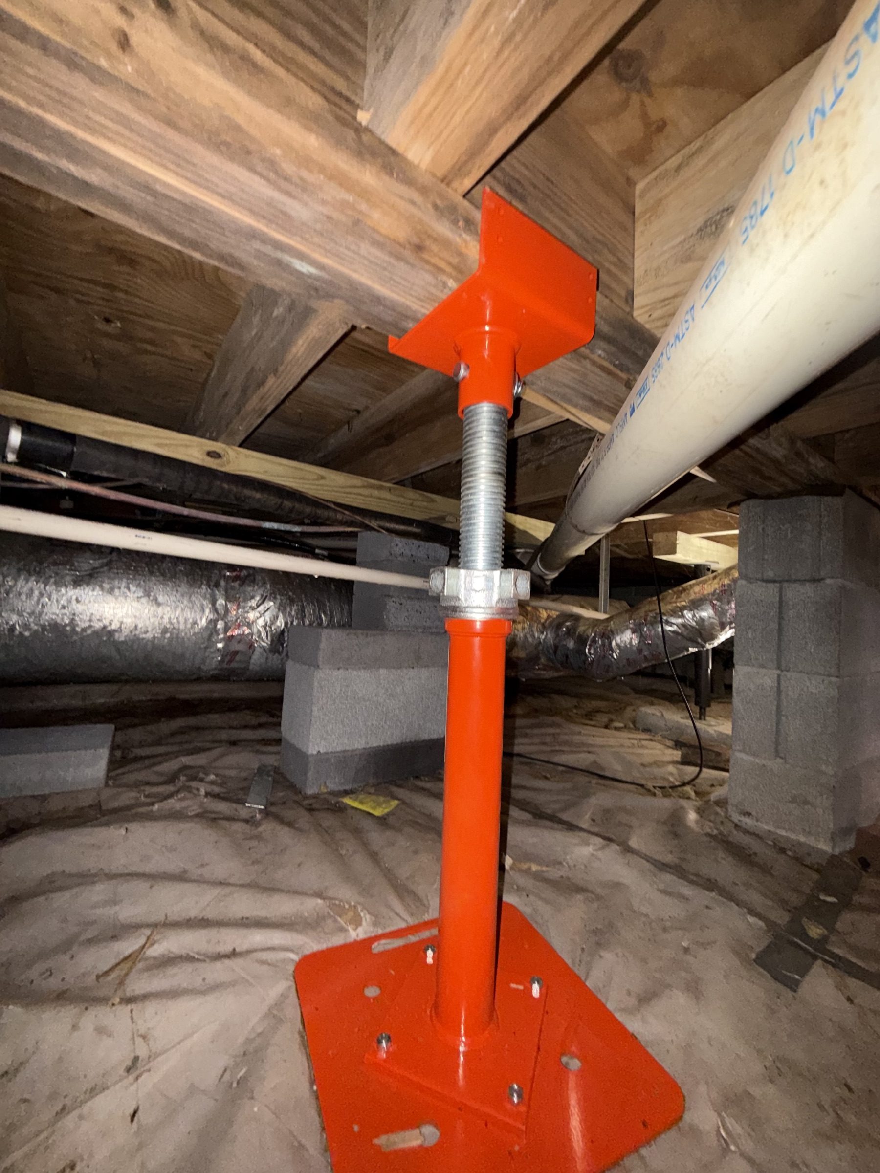 Adjustable steel jack post supporting floor joists in a crawlspace