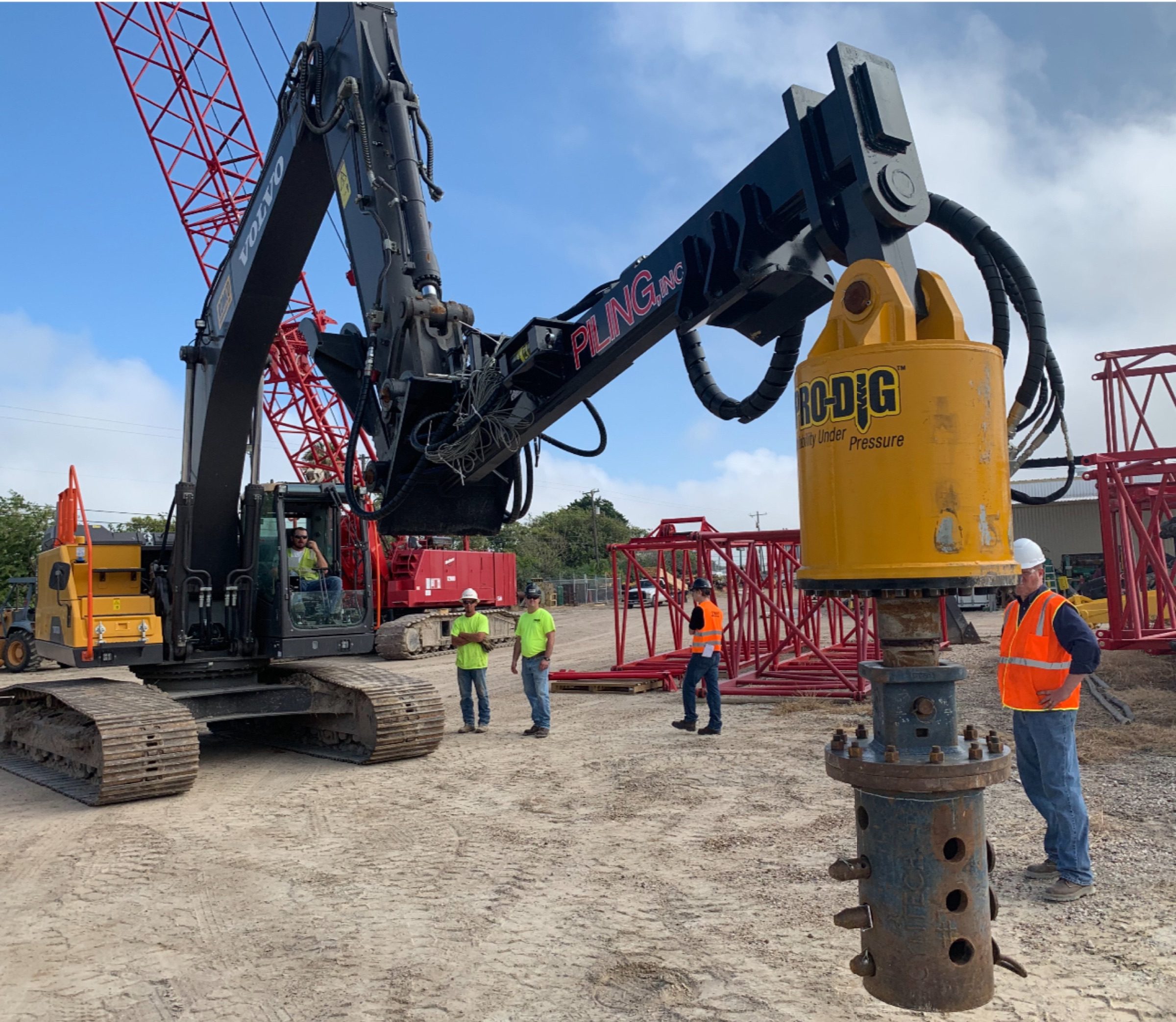 Excavator-mounted torque head and pile section in a yard