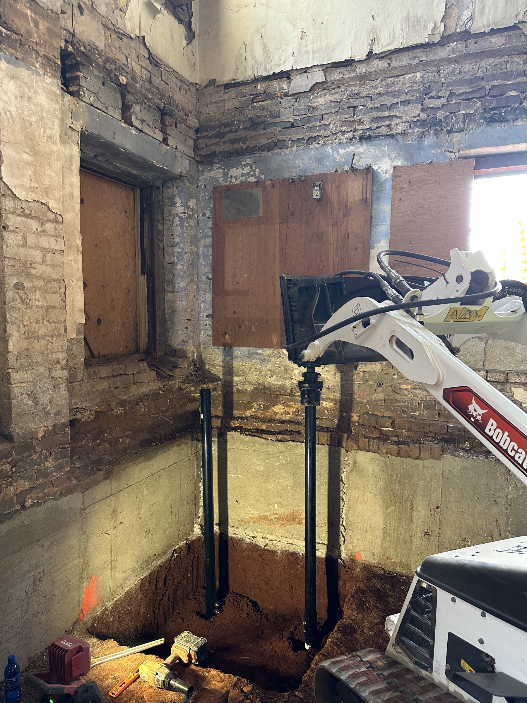 Interior underpinning piers standing in an open excavation in a historic brick basement